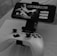 A mobile phone is mounted on a stand displaying a game titled 'Grimvalor' with options such as 'Continue', 'New Game', and 'Extras'. In front of the phone, there is a game controller placed on a table. The setup indicates gaming activity possibly using a smartphone as the screen.
